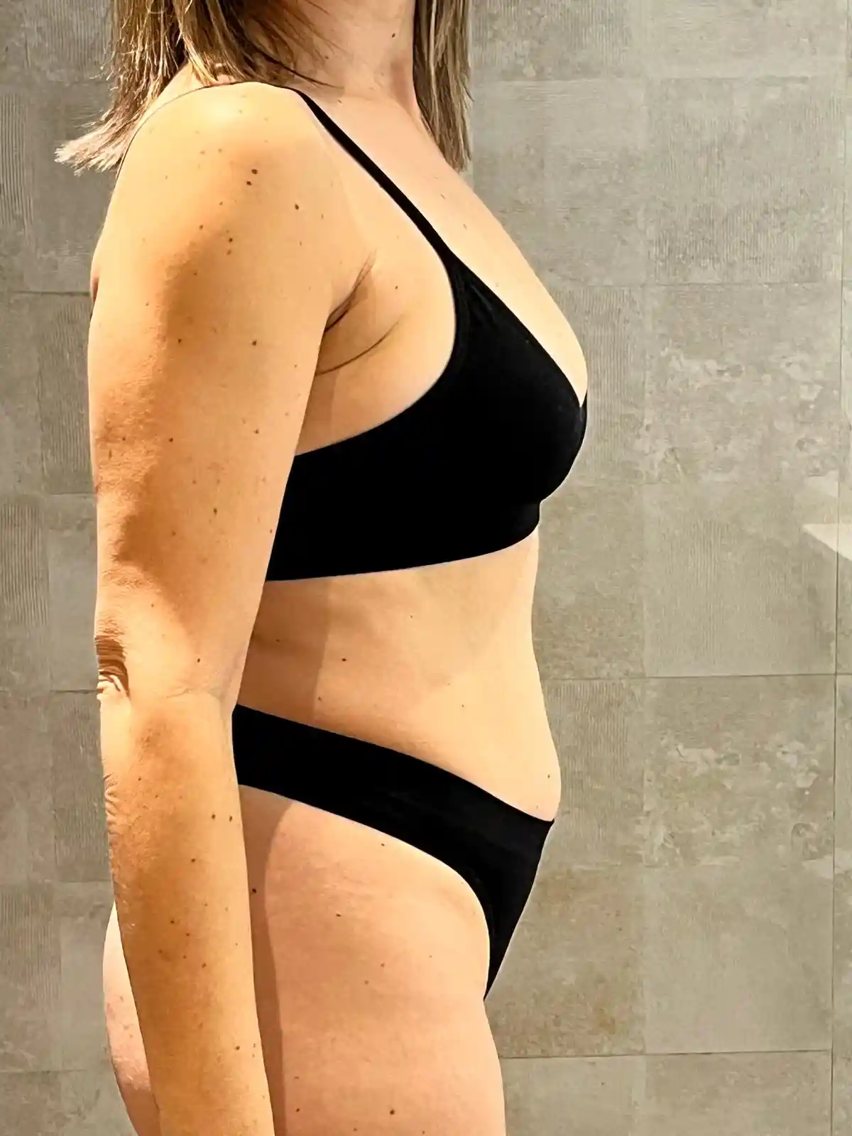 Antes de la transformación: mujer adulta en interior, perfil lateral, con ropa interior negra.